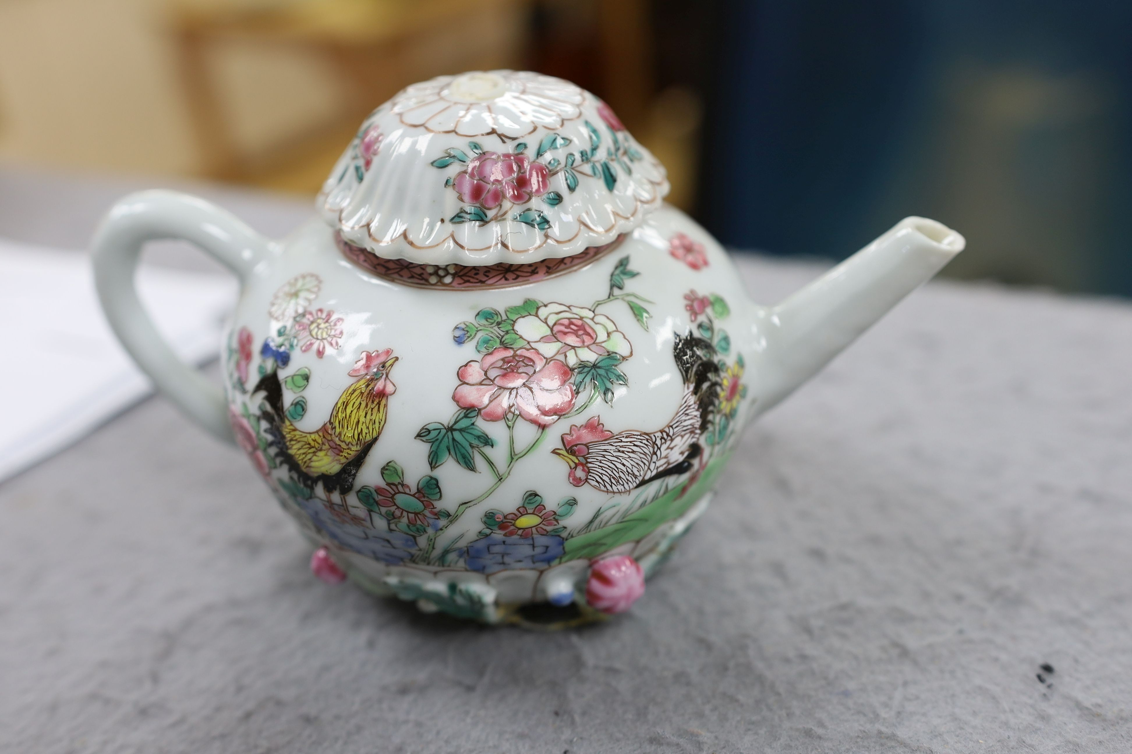 A Chinese famille rose chrysanthemum moulded teapot, early Qianlong period, painted with a cockerel amongst flowers, on a cage work base, 10 cms high